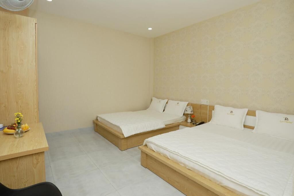 A hotel room with two single beds, a wooden desk, and a small table with a vase and fruit.