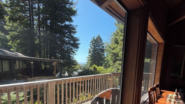 A wooden deck with a bench and table, overlooking a forested area. - Charming 2-bedroom country house in Fort Bragg with a view of Mckerriker Beach. (Fort Bragg)