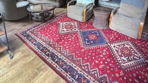 A cozy living room with wooden walls, a brick fireplace, and a large red patterned rug. - Charming 2-bedroom country house in Fort Bragg with a view of Mckerriker Beach. (Fort Bragg)