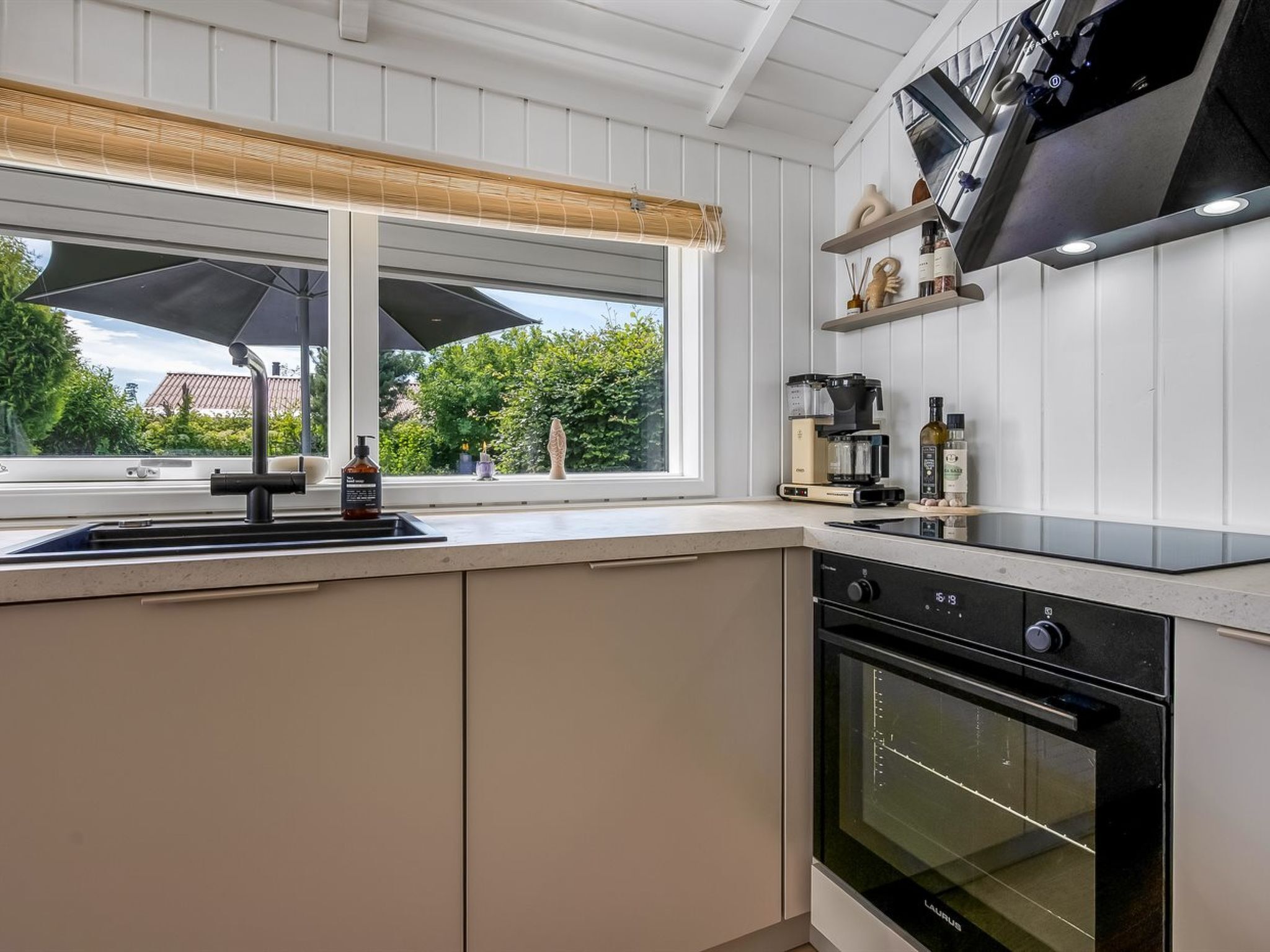 Una cocina con ventana, pileta, estufa y cafetera.