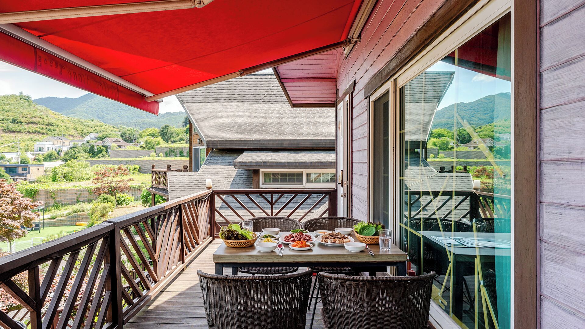 A balcony with a table set for dining, wicker chairs, and a red awning.