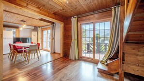 A wooden interior with a dining area, a kitchen, and a large window with curtains.