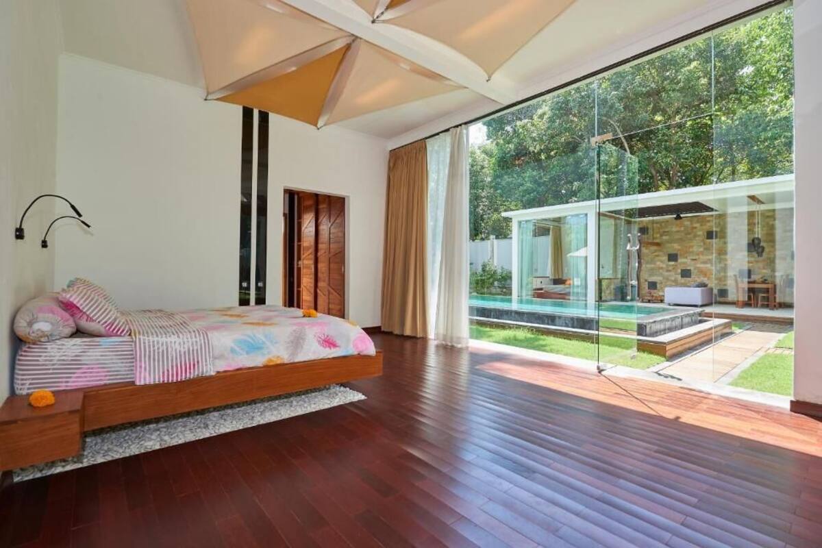 A modern bedroom with a large bed, a glass wall, and a view of a swimming pool.