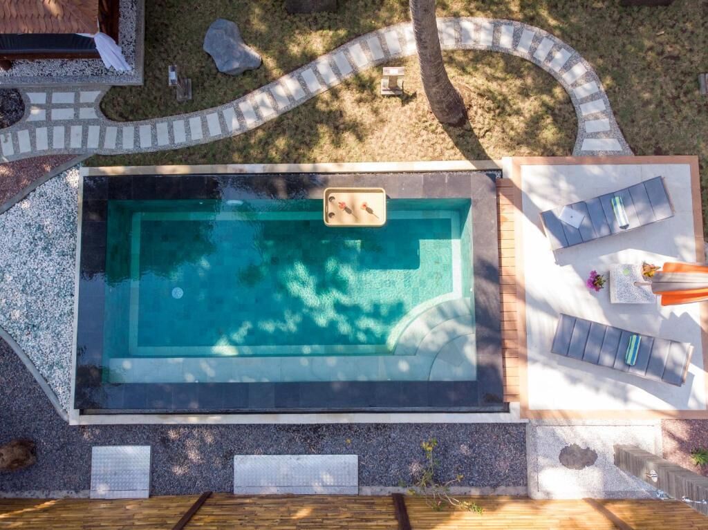 A rectangular swimming pool with a hot tub, surrounded by a deck, and a lounge area with chairs and a table.