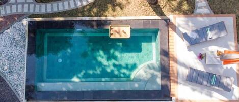 A rectangular swimming pool with a hot tub, surrounded by a deck, and a lounge area with chairs and a table.
