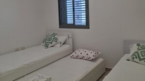 A room with two single beds, a window with blinds, a wall-mounted air conditioner, and a power outlet. - Keren Home 3 bedr Karmei Gat Kiriat Gat (Kiriat gat)