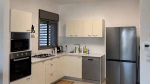 A modern kitchen with a built-in oven, microwave, gas stove, stainless steel refrigerator, and a window with blinds. - Keren Home 3 bedr Karmei Gat Kiriat Gat (Kiriat gat)
