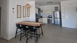 A modern kitchen with stainless steel appliances, a dining area with a wooden table and chairs, and a decorative wall piece. - Keren Home 3 bedr Karmei Gat Kiriat Gat (Kiriat gat)