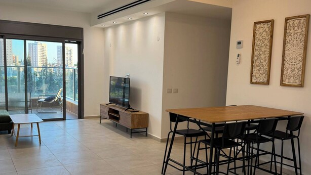 A modern living room with a dining area, large windows, and a TV. - Keren Home 3 bedr Karmei Gat Kiriat Gat (Kiriat gat)