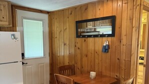 A compact kitchen with wooden walls, a white refrigerator, a dining table with chairs, and a mirror above the counter. - Dockside Cozy Cottage/Boat access/Spacious Yard/ sleeps 8 (Port Clinton)