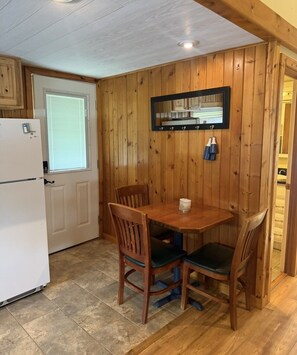 A compact kitchen with wooden walls, a white refrigerator, a dining table with chairs, and a mirror above the counter. - Dockside Cozy Cottage/Boat access/Spacious Yard/ sleeps 8 (Port Clinton)