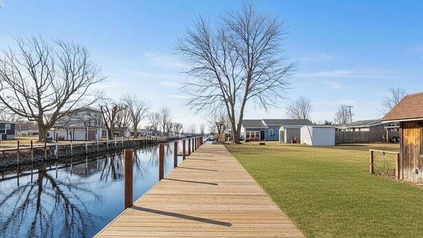 A wooden dock extending into a calm body of water, flanked by leafless trees and residential buildings. - Dockside Cozy Cottage/Boat access/Spacious Yard/ sleeps 8 (Port Clinton)