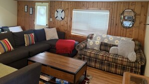 A cozy living room with a dark sofa, a plaid sofa, and a wooden coffee table. - Dockside Cozy Cottage/Boat access/Spacious Yard/ sleeps 8 (Port Clinton)