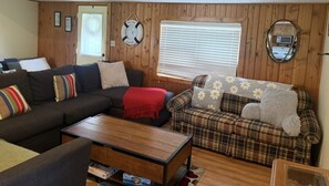 A cozy living room with a dark sofa, a plaid sofa, and a wooden coffee table. - Dockside Cozy Cottage/Boat access/Spacious Yard/ sleeps 8 (Port Clinton)
