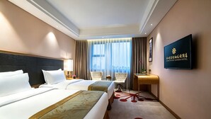 Habitación de hotel con dos camas, televisión, escritorio y vistas a la ciudad a través de amplias ventanas.