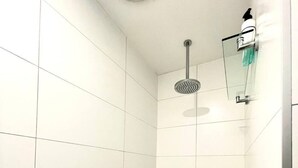 Een douche met een handdouche, een glazen zeepdispenser en een metalen handdoekhouder.