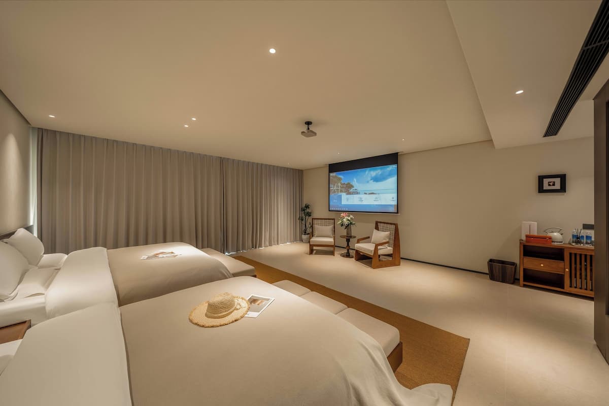 A hotel room with a large bed, a smaller bed, a sofa, a TV screen, and a desk with a chair.