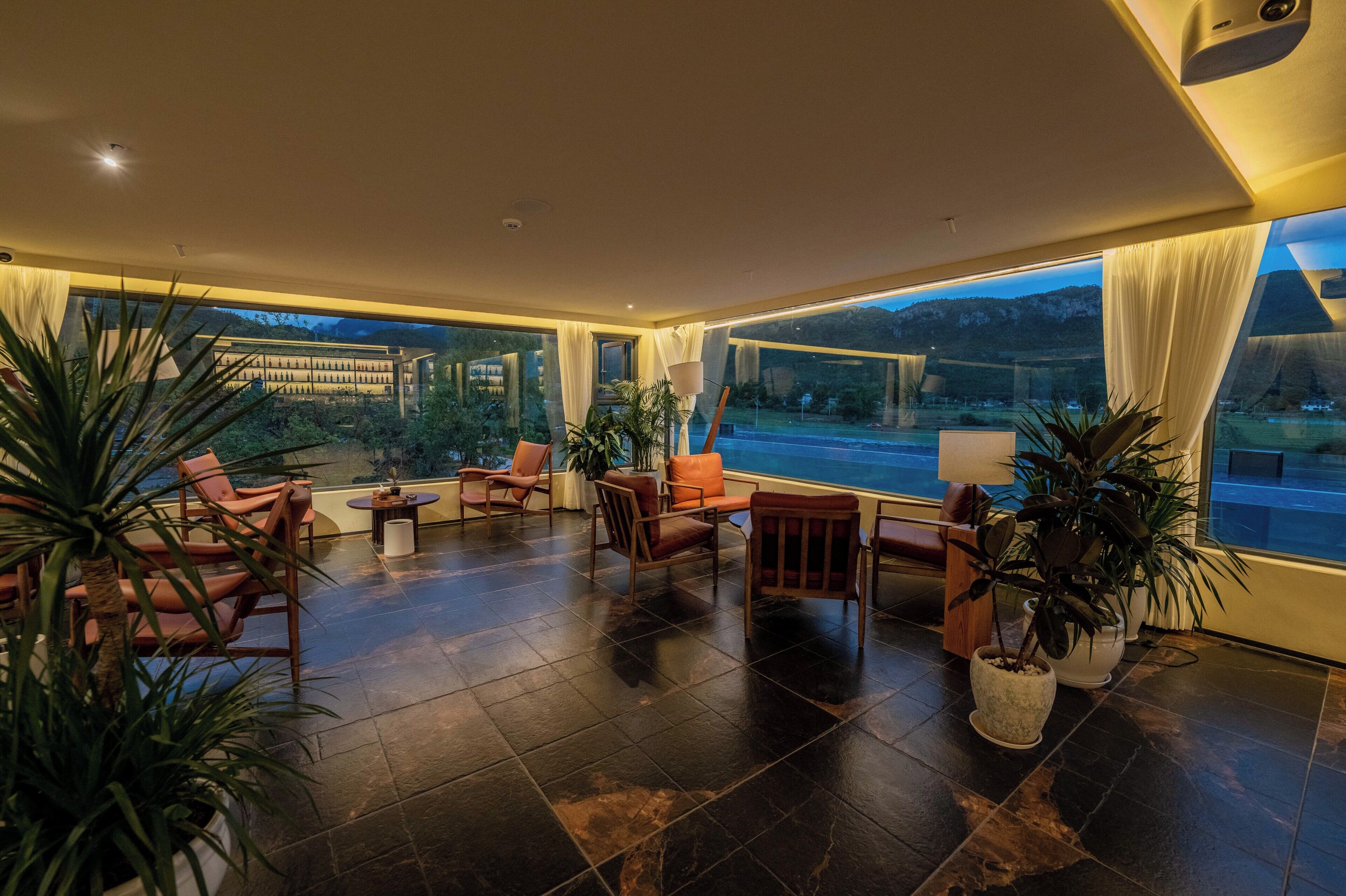 A spacious indoor area with large windows, seating arrangements, and potted plants.