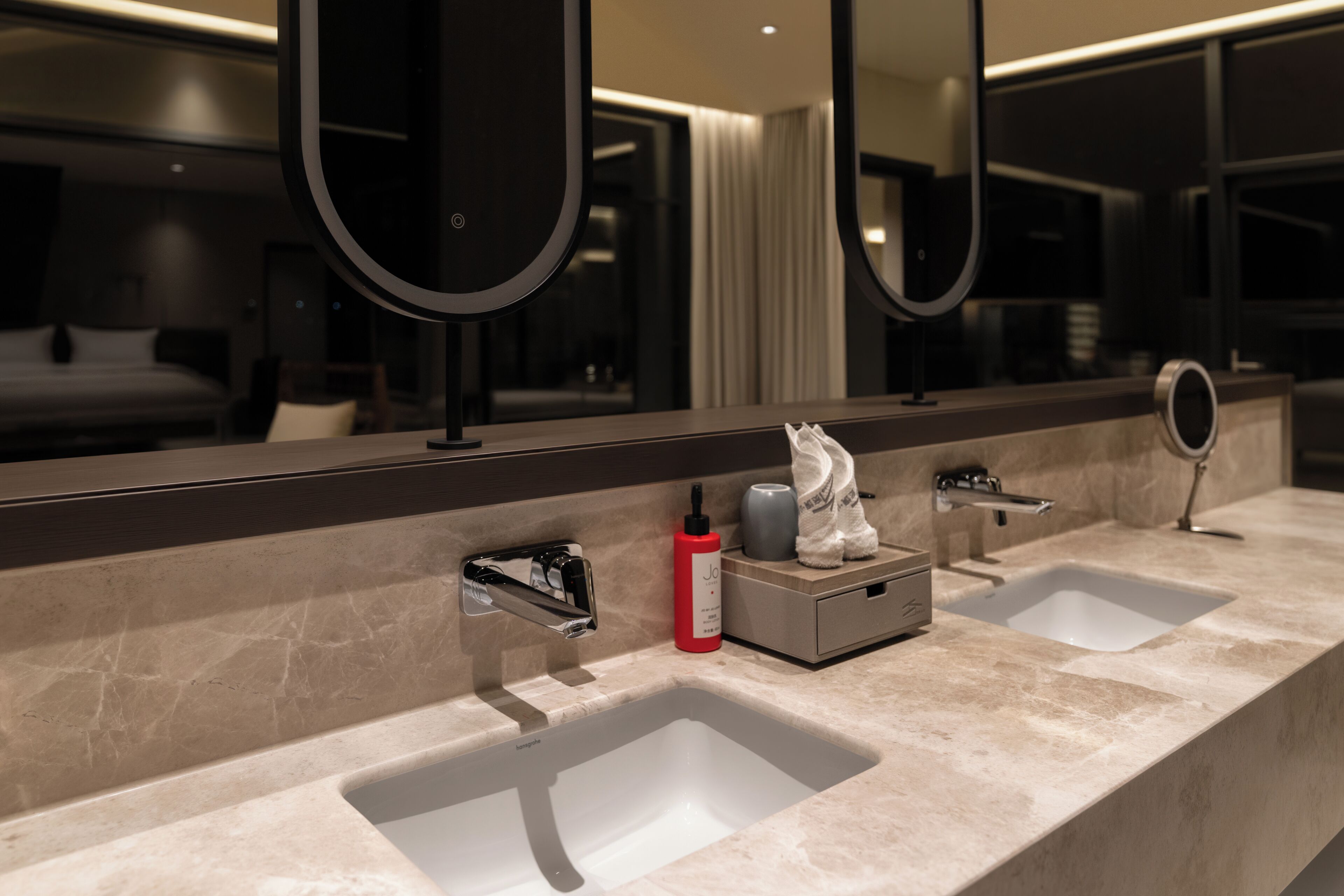A modern bathroom with two sinks, a large mirror, and a small cabinet.