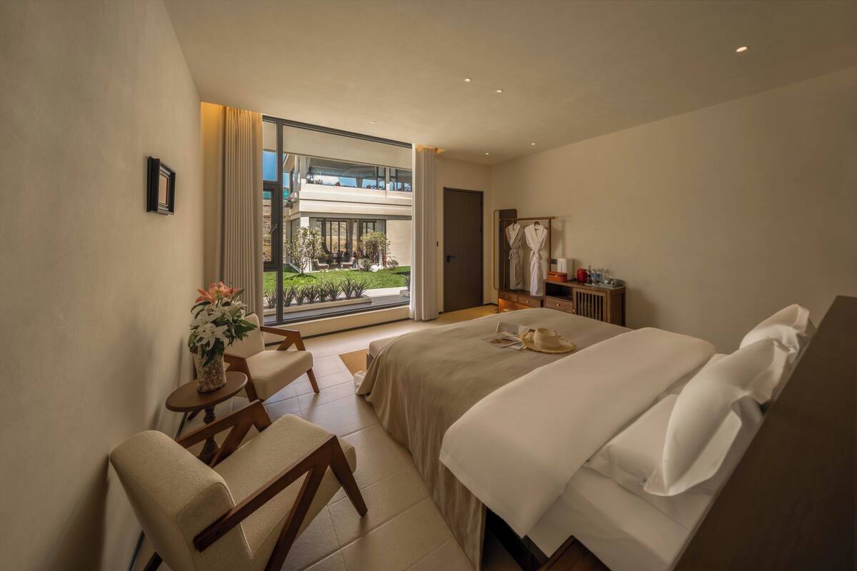 A modern hotel room with a large bed, a seating area, a view of the outdoors, and a balcony.