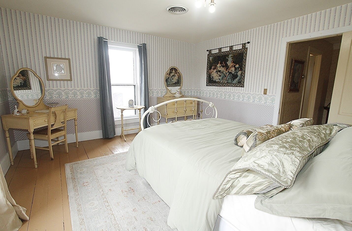 A bedroom with a bed, a vanity with a mirror, a dresser, and a window with curtains.
