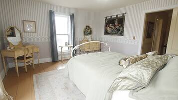 A bedroom with a bed, a vanity with a mirror, a dresser, and a window with curtains.