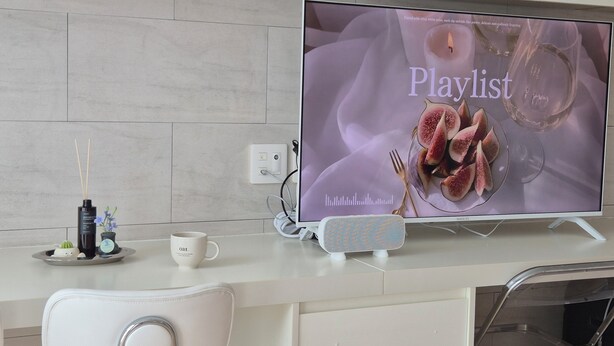Une cuisine moderne équipée d’un téléviseur à écran plat diffusant une liste de lecture, d’une chaise blanche, d’une petite table avec une tasse et d’une bouteille décorative.