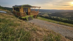 A small wooden cabin with a balcony, situated on a hill overlooking a valley. - Unusual caravan, sunset with vineyards in the Ain valley (SAINT-ALBAN)