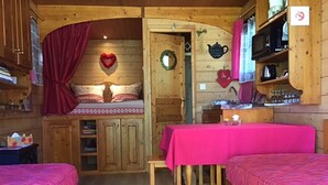 A cozy cabin-style room with two beds, a small table, and a kitchenette. - Unusual caravan, sunset with vineyards in the Ain valley (SAINT-ALBAN)