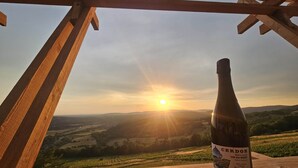 A bottle of Cerdon wine on a wooden table with a scenic view of a valley and the sun setting in the background. - Unusual caravan, sunset with vineyards in the Ain valley (SAINT-ALBAN)