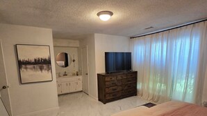 A bedroom with a bed, a dresser, a TV, a mirror, and a painting on the wall.