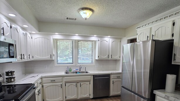 A modern kitchen with white cabinets, stainless steel appliances, and a wooden floor.