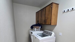 A laundry room with a washing machine, dryer, wooden cabinet, and a laundry basket on the floor.