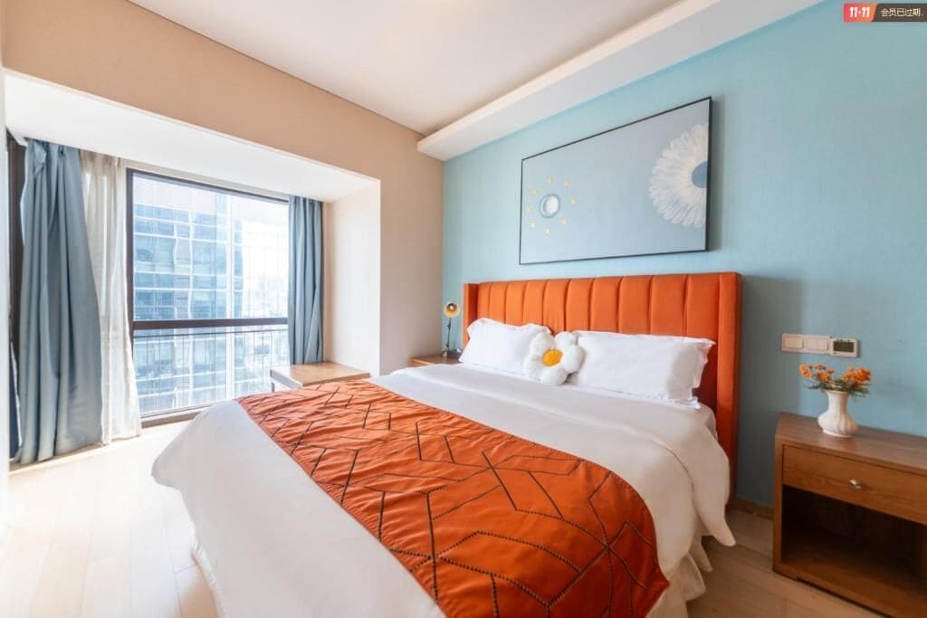 Una habitación de hotel con una cama grande, una mesita de noche, una ventana con cortinas y un reloj en la pared.