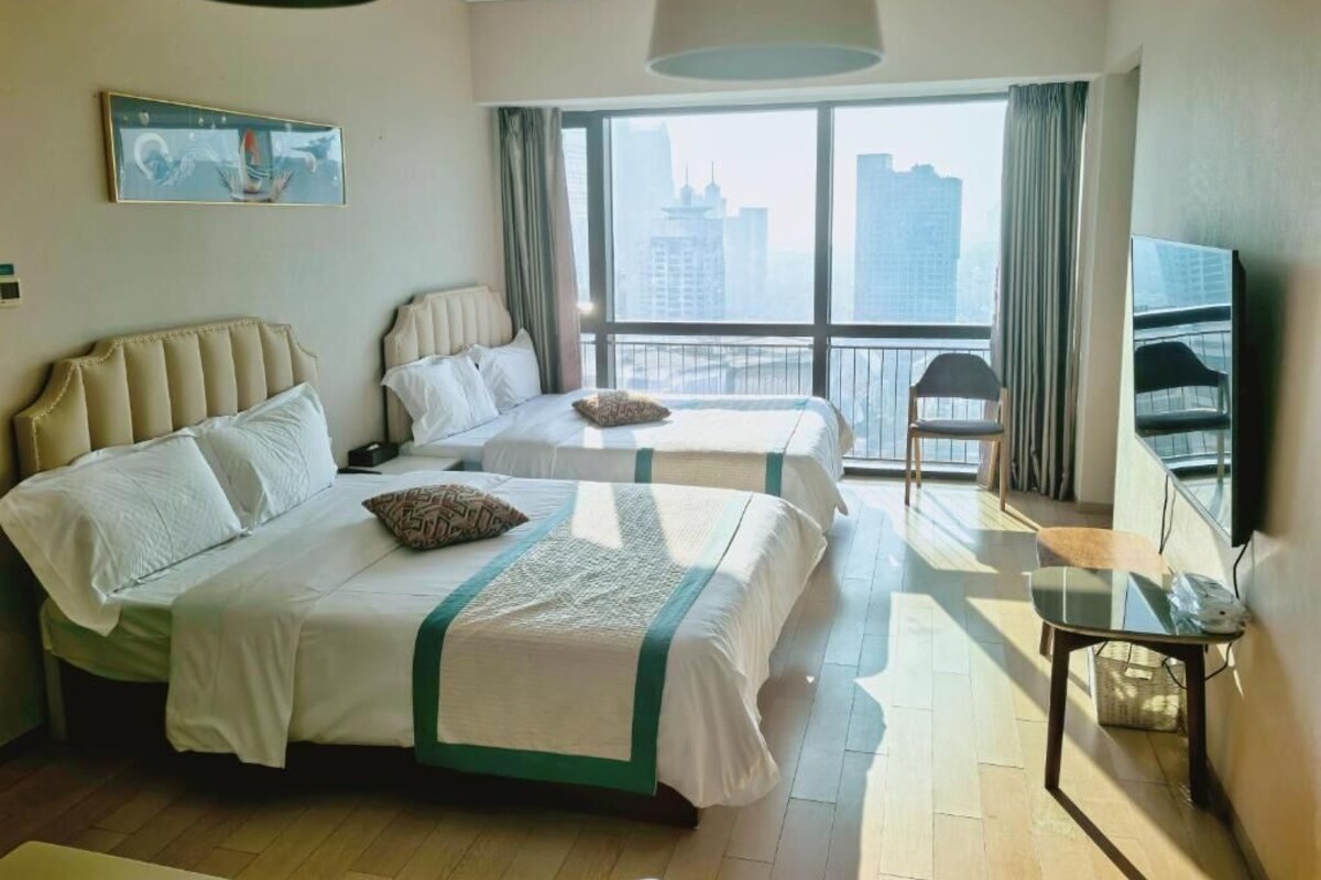 Habitación de hotel con dos camas, televisión, balcón y vista a la ciudad.