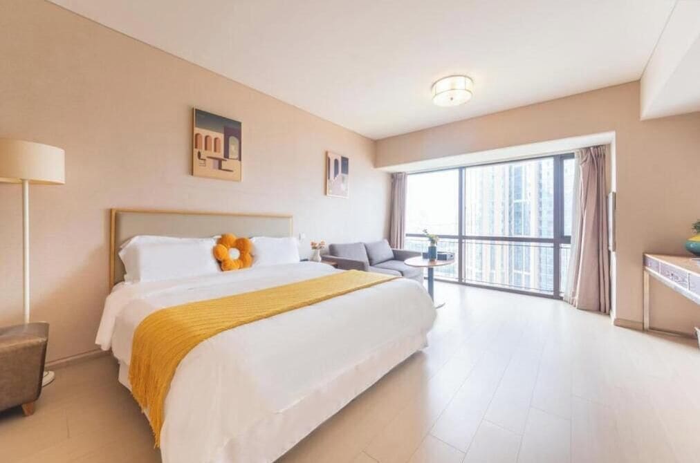 Habitación de hotel con una cama grande, un escritorio, una silla y vista a la ciudad por la ventana.