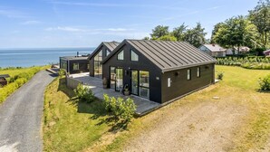 Ett modernt hus med en stor glasdörr, en asfalterad uppfart och utsikt över havet.