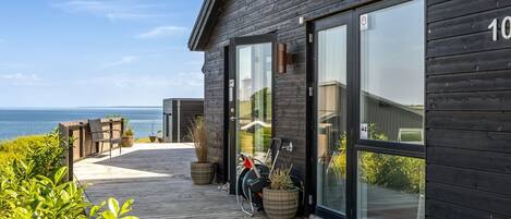 A modern wooden building with large glass doors, a wooden deck, and a view of the sea.