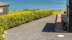 En fastighet vid kusten med en grusuppfart som leder till en träveranda, en liten byggnad och utsikt över havet.