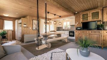 L’intérieur chaleureux d’un chalet avec un plafond en bois, un coin repas, une cuisine et un salon comprenant un canapé et une table basse.