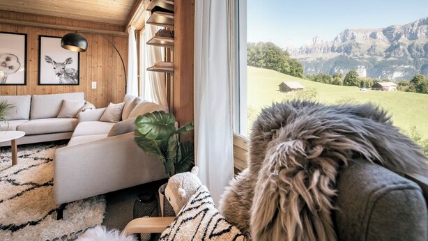 A cozy living room with a sofa, a coffee table, and a large window offering a view of a mountainous landscape. - Chalet Agathli, (Flumserberg Bergheim), by Interhome (Flumserberg Bergheim)