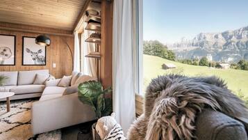 Un salon chaleureux avec un canapé, une table basse et une grande fenêtre donnant sur un paysage montagneux.