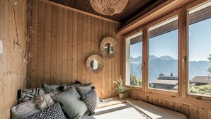 A wooden room with a bed, two wall mirrors, and a view of mountains through large windows. - Chalet Agathli, (Flumserberg Bergheim), by Interhome (Flumserberg Bergheim)