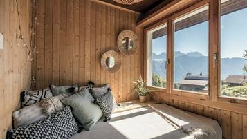 Une pièce en bois avec un lit, deux miroirs muraux et une vue sur les montagnes, visible à travers de grandes fenêtres.