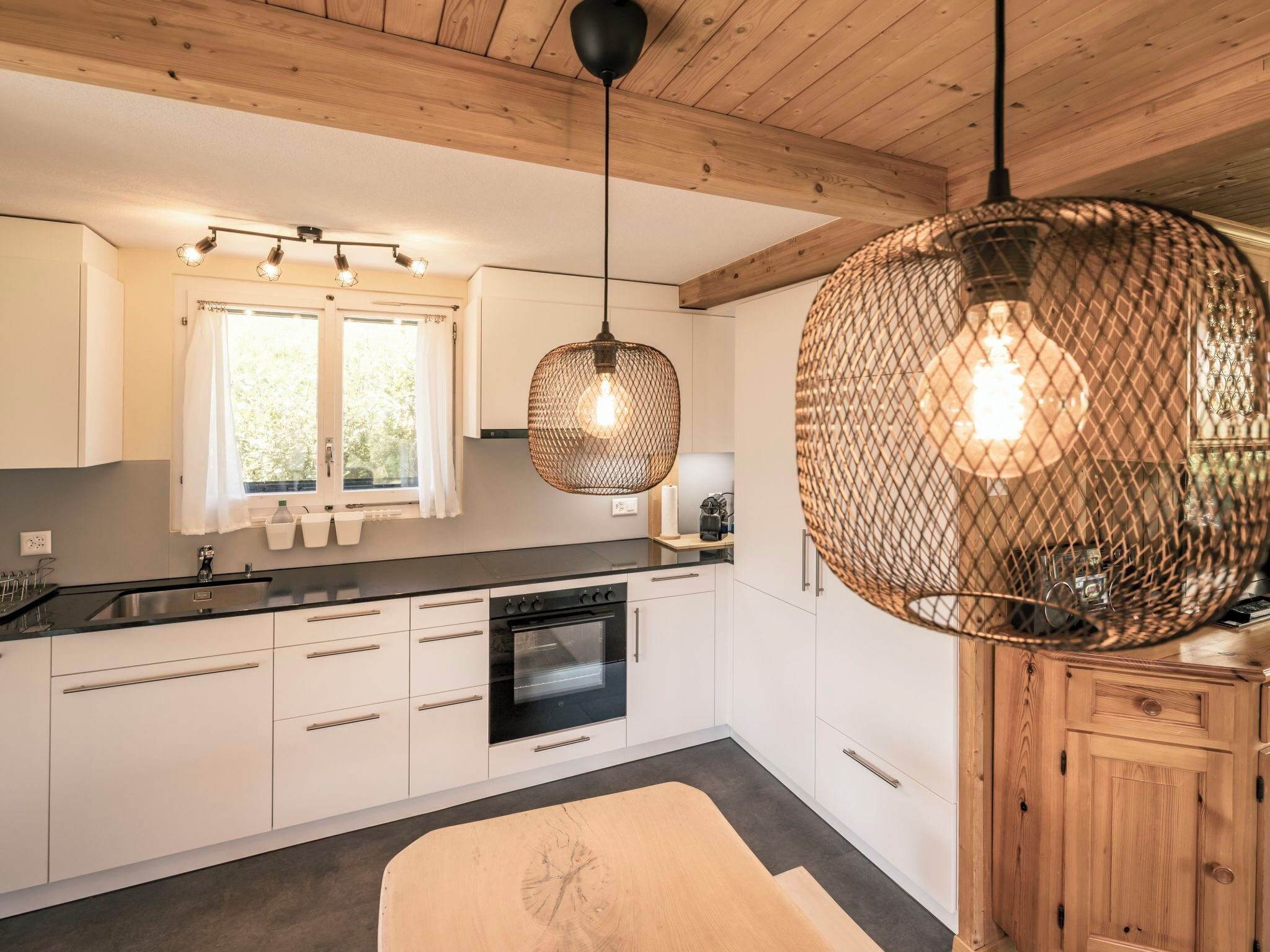 Une cuisine moderne avec des armoires blanches, un comptoir noir, un four encastré et un grand luminaire suspendu.