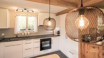 Une cuisine moderne avec des armoires blanches, un comptoir noir, un four encastré et un grand luminaire suspendu.