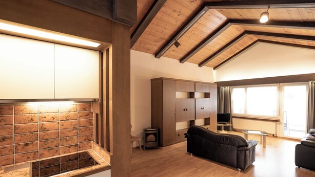 Ein geräumiger Wohnbereich mit Küche, Holzbalken an der Decke und einem großen Fenster.