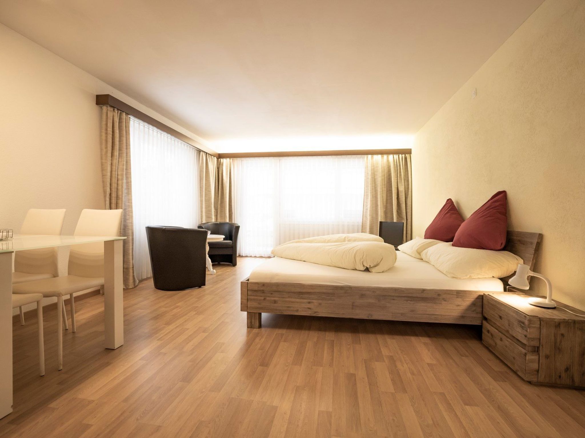 A hotel room with a bed, bedside table, lamp, and a desk with chairs.
