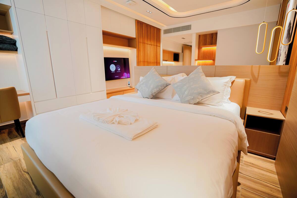 A modern hotel room with a large bed, a flat-screen TV, a wooden nightstand, and a built-in wardrobe.