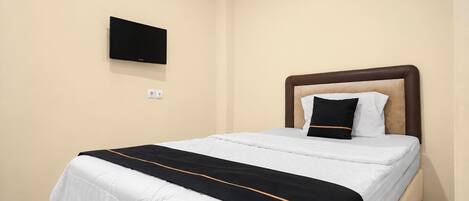 A hotel room with a bed, a flat-screen TV mounted on the wall, and a plain wall.